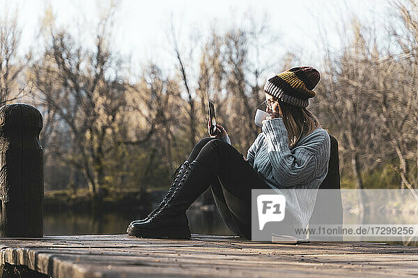 Frauen entspannen sich auf dem Holzsteg am See mit ihrem Smartphone.