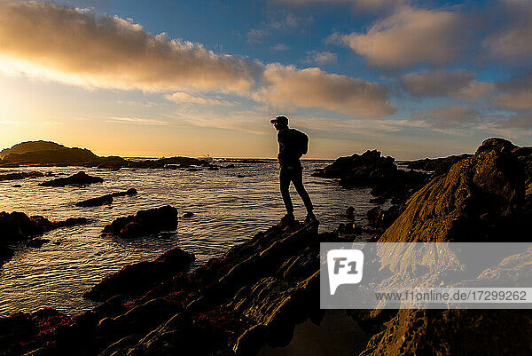 Silhouetted figure standing on shore with dramatic sunset in sky