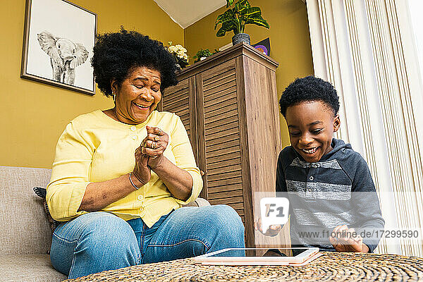 Fröhlicher Junge und Großmutter spielen ein Videospiel auf einem digitalen Tablet zu Hause