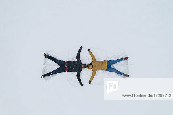 Junge kaukasische Paar tun Schnee Engel in einem weißen Schneefeld Winter