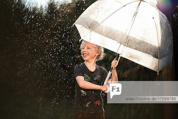 Glückliches Kind spielt im Regen unter Regenschirm