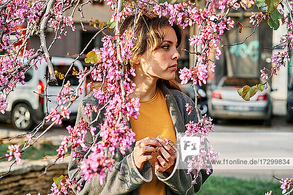 Junges Mädchen berührt die rosa Blüten des Baumes im Frühling