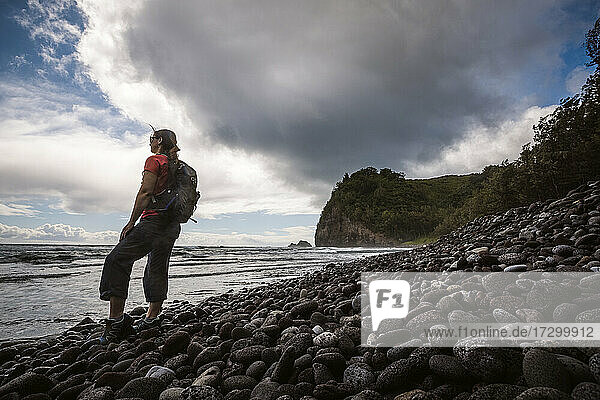 female hiker with backpack on Pololu Beach  Hawaii looks at Pacific.