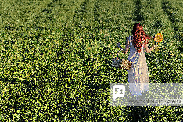 Weiß gekleidete Frau mit Weidenkorb und einer Sonnenblume im Gras