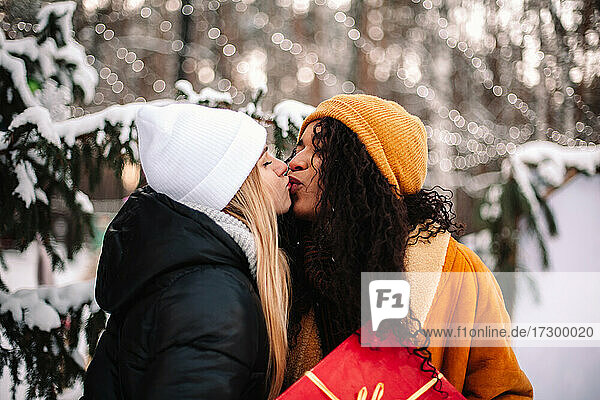 Glückliche Freundinnen  die sich küssen und ein Weihnachtsgeschenk unter dem Weihnachtsbaum halten