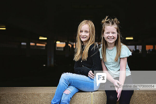 Two happy tween girls sitting on a brick wall together.