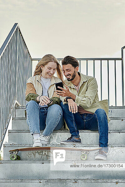 Junges gemischtrassiges Paar lächelt  während sie auf ein Telefon schauen