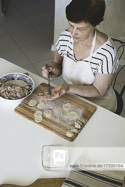 Eine Frau in einer weißen Küche bereitet traditionelle russische Knödel aus Fleisch und Teig zu