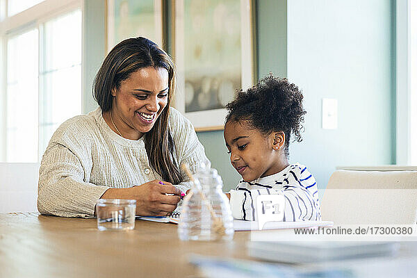 Glückliche Mutter bringt ihrer Tochter am Tisch sitzend das Zeichnen bei