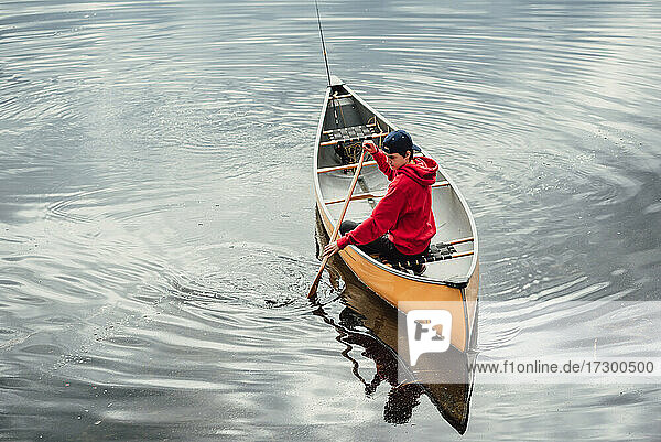 Ein Jugendlicher paddelt allein mit einem Kanu auf einem ruhigen See in Kanada.
