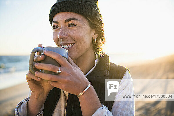 Young woman enjoying drink in mug while beach car camping alone