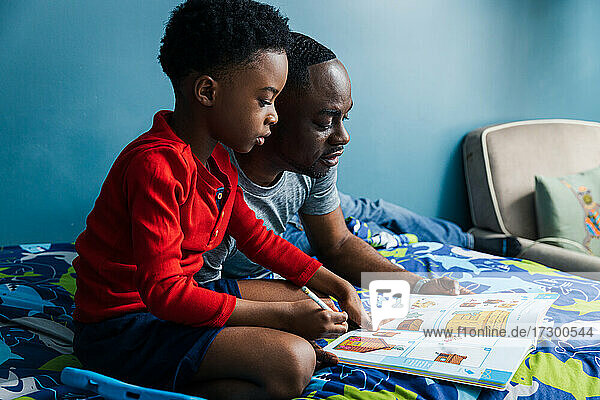 Vater hilft Sohn bei den Hausaufgaben auf dem Bett zu Hause