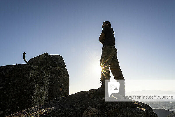 Silhouette of man standing on rocky mountain top near sunset time