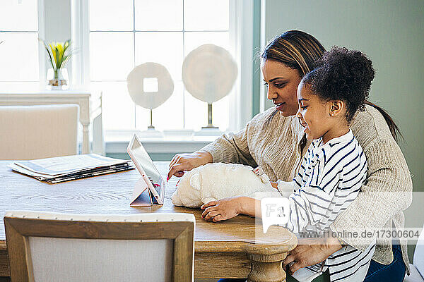Niedliche Tochter mit Mutter  die zu Hause ein digitales Tablet benutzt