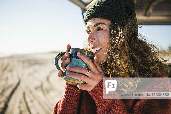 Junge Frau genießt eine Tasse Kaffee am Morgen am Strand Auto Camping