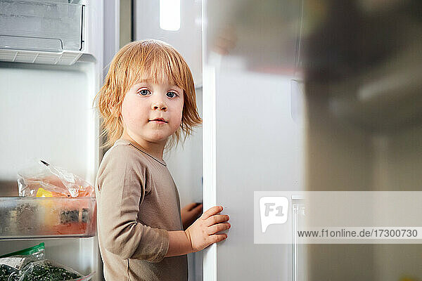 rothaariger Junge schaut in den Kühlschrank