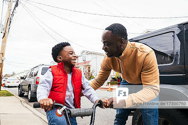 Smiling father teaching happy son to ride a bike outside at home