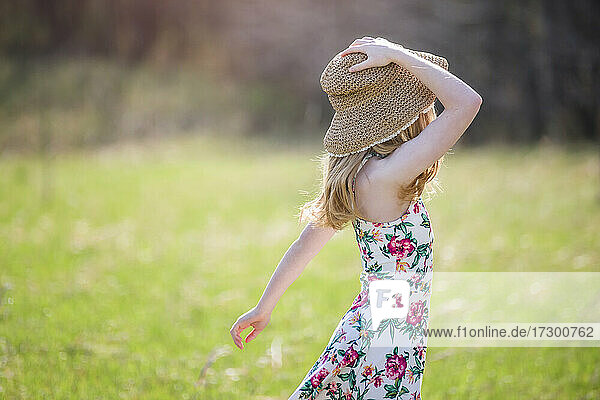 Schönes blondes Teenager-Mädchen im Freien in Sonnenkleid und Sonnenhut  von hinten beleuchtet.