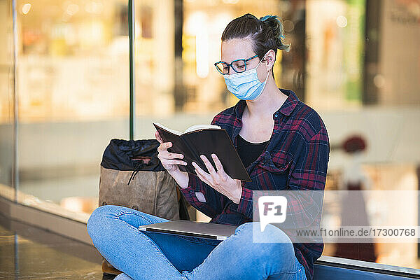 Spanische Frau mit Maskenbrille und Rucksack  lesend mit Laptop in der Ma