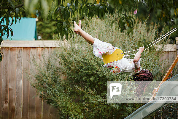 ein barfuß gehendes Kind schaukelt hoch auf einem Spielbrett in einem Hinterhofgarten