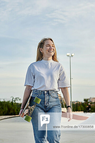 Junge blonde Frau lächelt und hat Spaß mit einem Skateboard