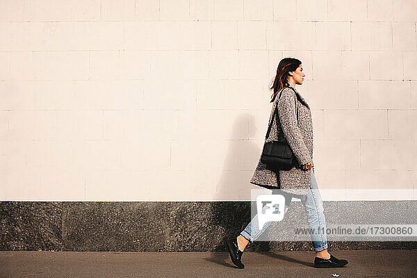 Side view of woman walking against wall in city