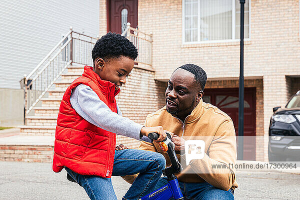 Vater hilft seinem Sohn  auf der Straße Fahrrad zu fahren