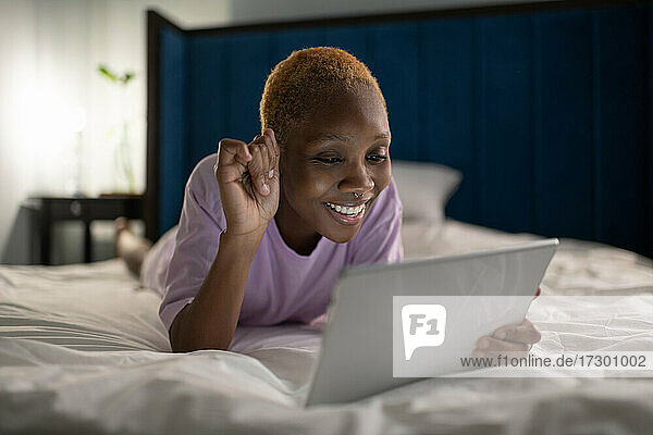 Glückliche Frau auf dem Bett liegend und mit Videoanruf auf Tablet