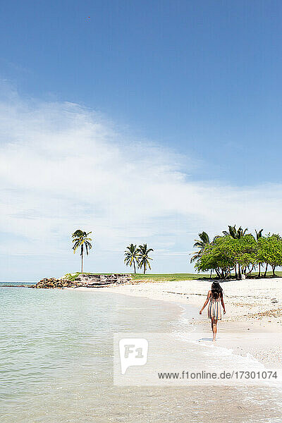 Junge Frau im Sommerkleid  die am Strand mit Palmen entlangläuft