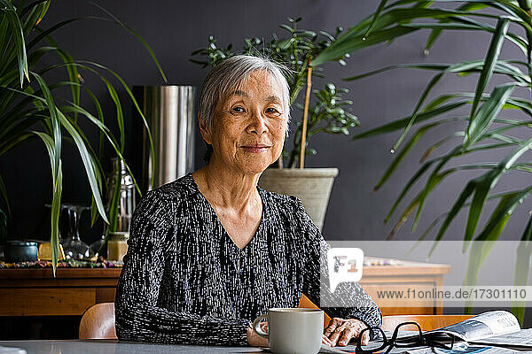 Porträt der lächelnden asiatischen Senior Frau sitzt am Tisch zu Hause