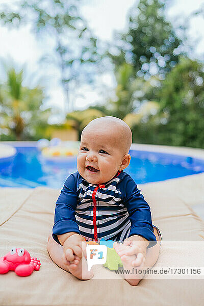 Cute Little Baby Sitting neben einem Pool spielen mit einem Spielzeug
