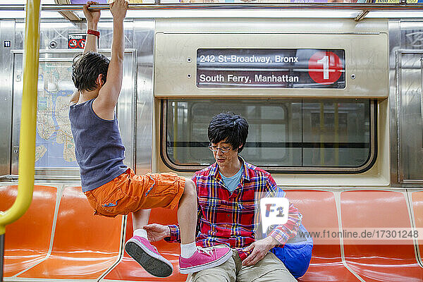 Kleiner Junge hängt an einem Geländer in der New Yorker U-Bahn und sein Vater zieht ihn herunter