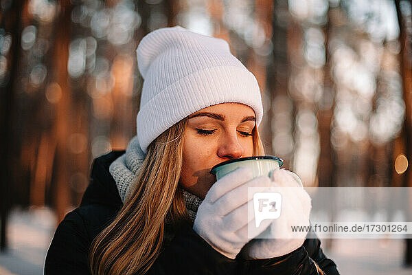 Frau hält Tasse und genießt heißes Getränk im Freien im Winter