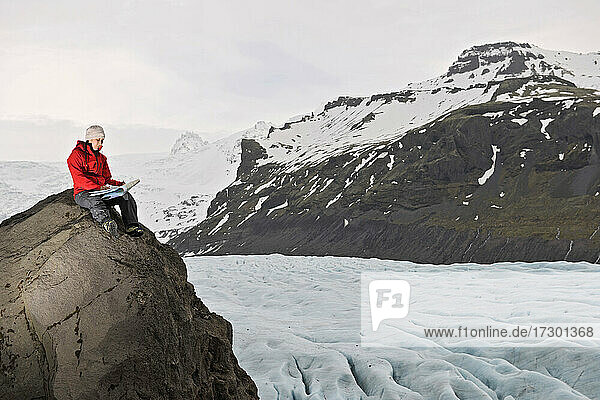 Female hiker reading map on rock above glacier