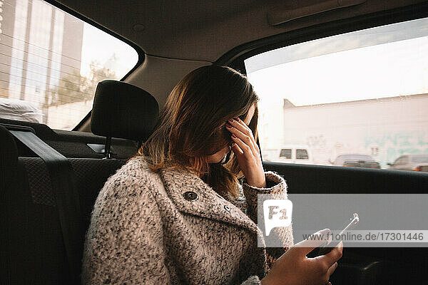 Frau  die ihr Gesicht bedeckt und lachend ihr Smartphone im Auto hält