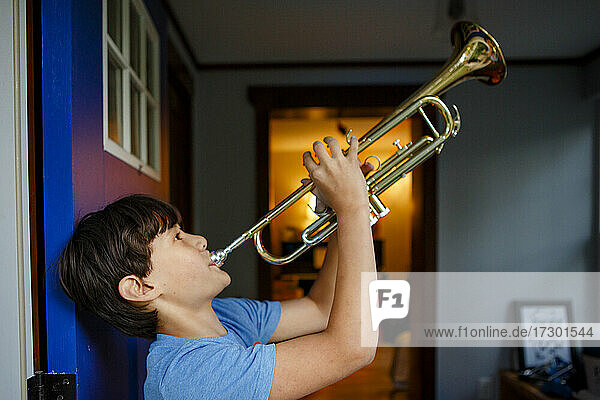 Ein Junge steht in einer bunten offenen Tür und spielt Trompete