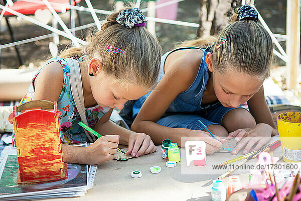 Mädchen malen mit Farben auf Holzrohlinge. Straßenkunstfestival