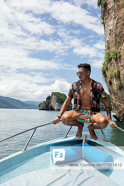 Young stylish man sitting on front of boat in the ocean