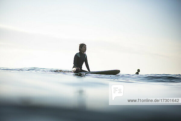 Asiatische Frau wartet auf Wellen während Sonnenaufgang Sommer Surf-Session