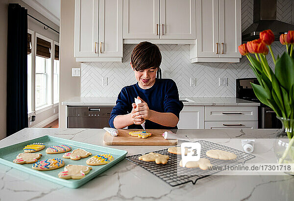 Junger Junge beim Verzieren von Osterkeksen auf dem Tresen einer modernen Küche.