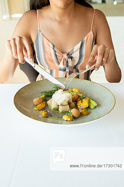 Junge Frau hält Essbesteck über einem Teller mit feinen Speisen