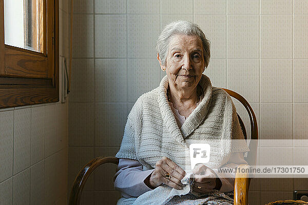 Großmutter näht mit Nadel und Faden und schaut dabei in die Kamera