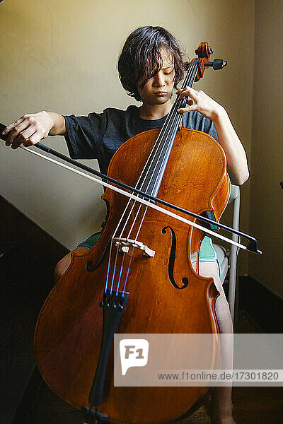 Nahaufnahme eines Jungen  der konzentriert Cello spielt  in einem Treppenhaus