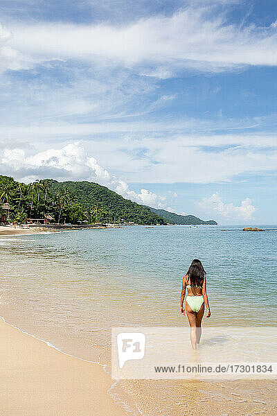 Junge Frau geht im grünen Bikini am Strand entlang