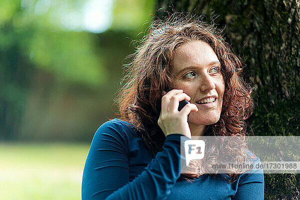 Junge Frau beim Abhören eines Smartphones im Freien