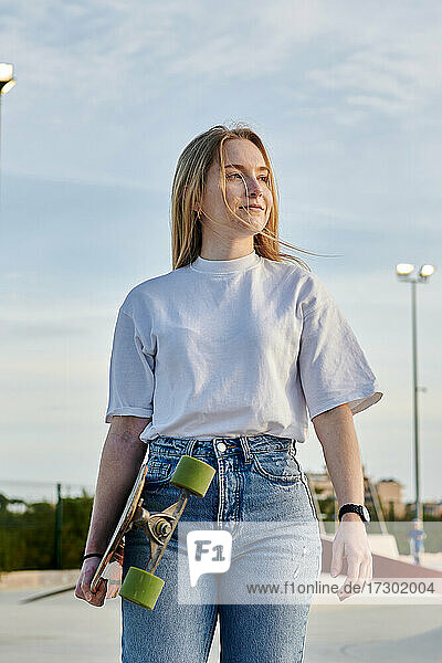 Young blonde woman smiling and having fun holding a skateboard