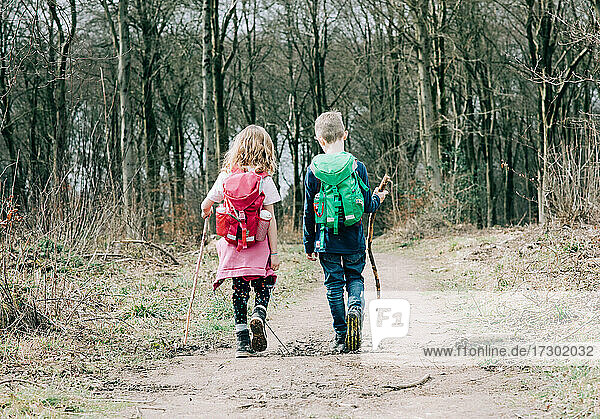 two kids hiking together with sticks and backpacks talking in the UK