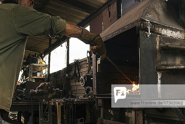 Blacksmith stoking a forge fire in his workshop.