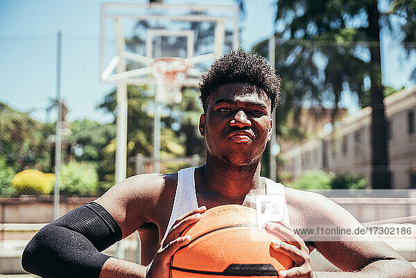 Porträt eines wütenden schwarzen Afro-Jungen mit trotzigem Blick  der den Basketball mit seinen Händen zusammendrückt. Bereit  ein Spiel zu spielen.