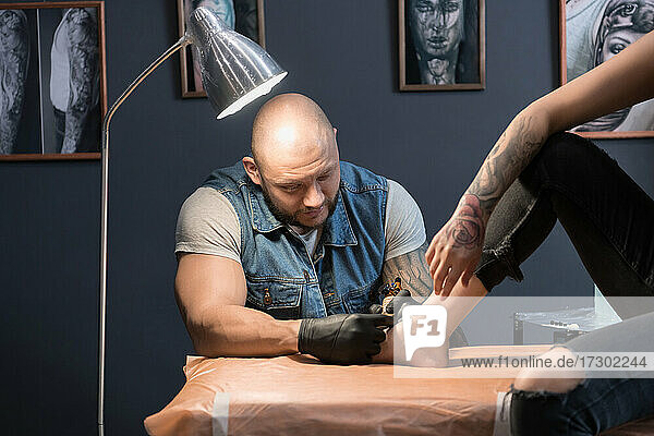 Glatzköpfiger Mann macht Tattoo auf Fuß der Frau